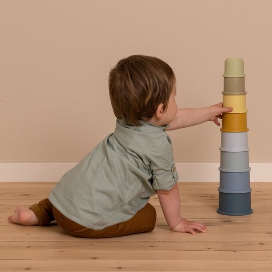 Kind speelt op de grond met de acht stapelbekers van diverse kleuren blauw, oranje, lichtgeel, taupe en lichtgroen.