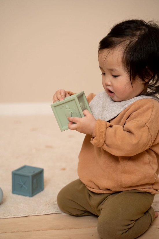 Kind speelt op de grond met 2 siliconen blokken in de kleur donkerblauw met zeester afdruk en lichtgroen met schildpad afdruk.